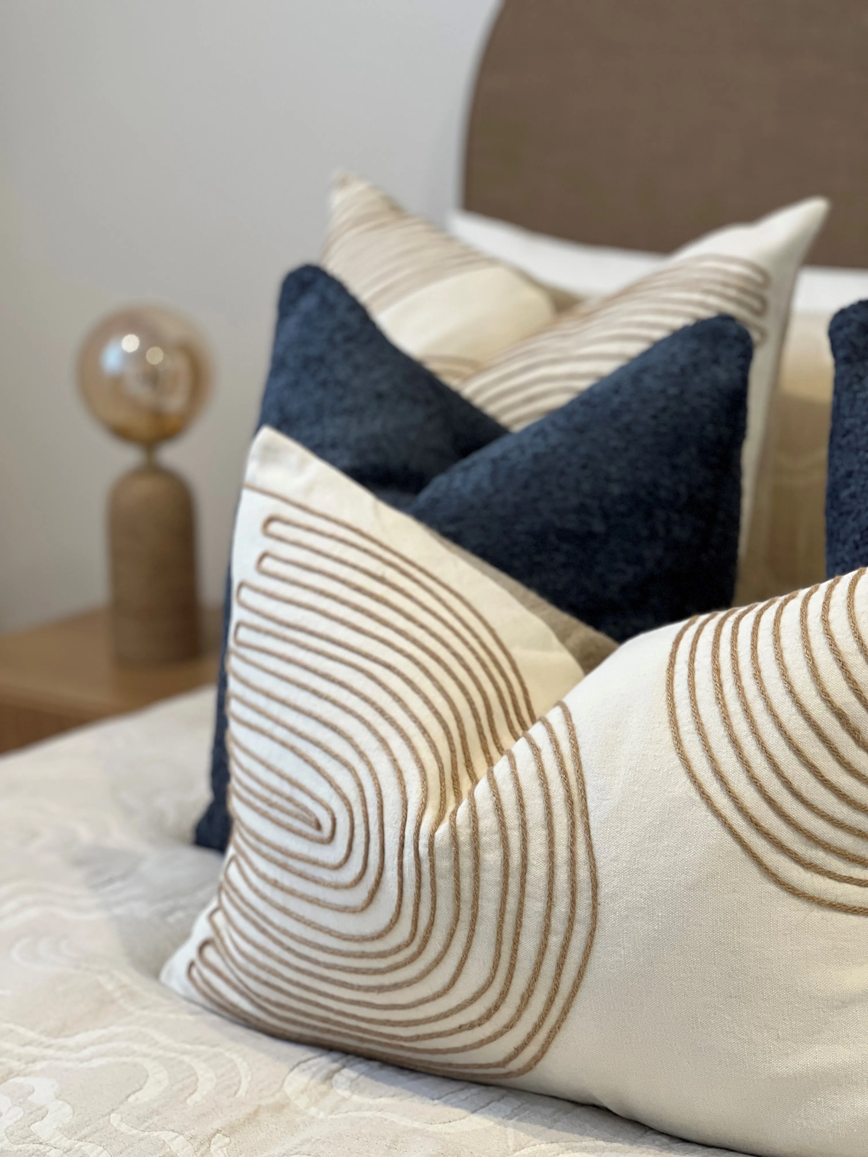 Guest bedroom cushion detail with embroidered arches and navy bouclé